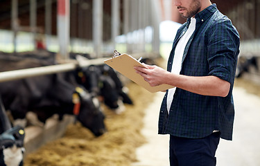 Image showing farmer with clipboard and cows in cowshed on farm