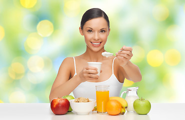 Image showing happy woman with fruits, cereals eating yogurt