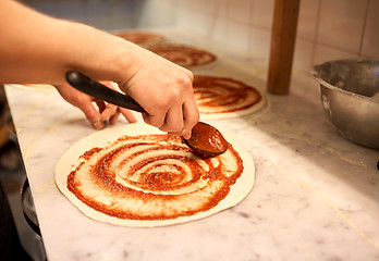 Image showing cook applying tomato sauce to pizza at pizzeria