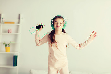 Image showing girl jumping on bed with smartphone and headphones