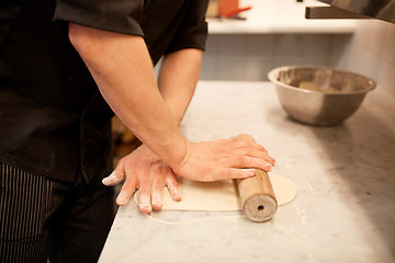 Image showing chef with rolling-pin rolling dough at kitchen