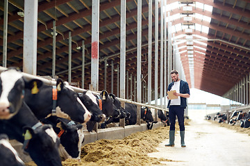 Image showing farmer with clipboard and cows in cowshed on farm