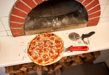 Image showing baked pizza on peel and cutter at pizzeria oven 