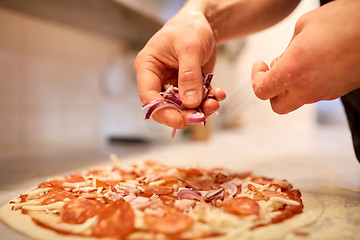 Image showing cook adding onion to salami pizza at pizzeria