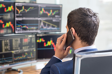 Image showing Over the shoulder view of stock broker trading online, talking on mobile phone.