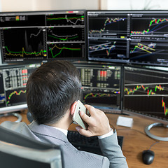 Image showing Over the shoulder view of stock broker trading online, talking on mobile phone.