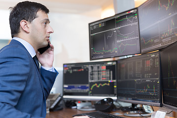 Image showing Stock broker trading online, talking on mobile phone.