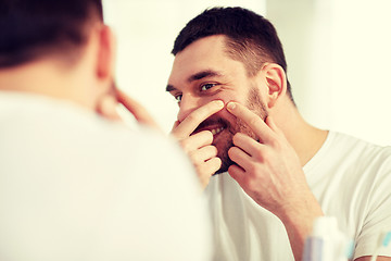 Image showing smiling man squeezing pimple at bathroom mirror