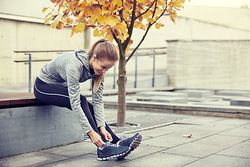 Image showing happy young sporty woman tying shoelaces outdoors