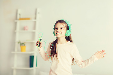 Image showing girl jumping on bed with smartphone and headphones