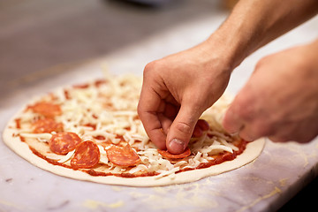 Image showing cook hands adding salami to pizza at pizzeria