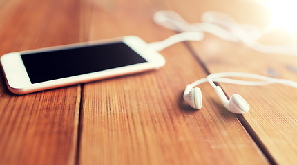 Image showing close up of blank smartphone and earphones on wood