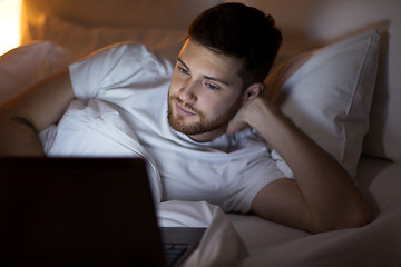 Image showing young man with laptop in bed at home bedroom