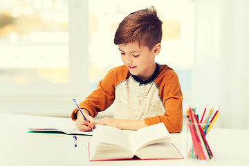 Image showing smiling student boy writing to notebook at home