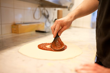 Image showing cook applying tomato sauce to pizza at pizzeria