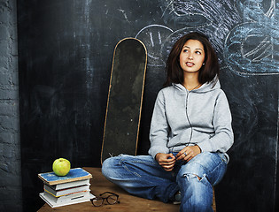 Image showing young cute teenage girl in classroom at blackboard seating on ta