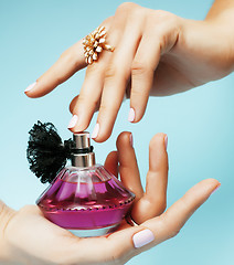Image showing woman hands holding bottle of perfume pink manicure and jewelry on blue background, luxury concept