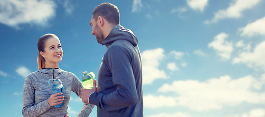 Image showing smiling couple with bottles of water over blue sky