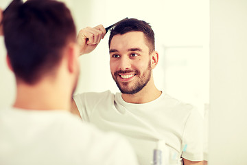 Image showing happy man brushing hair  with comb at bathroom