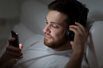 Image showing man with smartphone and headphones in bed at night