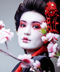 Image showing young pretty geisha in black kimono among sakura, asian ethno close up