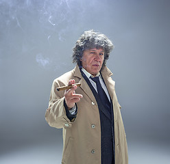 Image showing The senior man with cigar as detective or boss of mafia on gray studio background