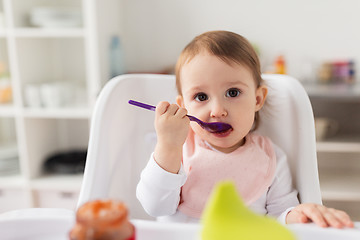 Image showing baby girl with spoon eating puree from jar at home