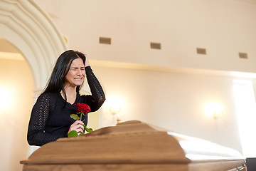 Image showing crying woman with red rose and coffin at funeral