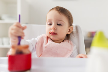 Image showing baby girl with spoon eating puree from jar at home