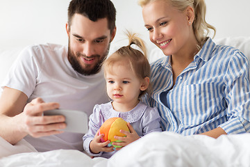 Image showing happy family with smartphone in bed at home