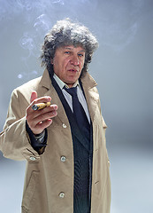 Image showing The senior man with cigar as detective or boss of mafia on gray studio background