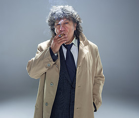 Image showing The senior man with cigar as detective or boss of mafia on gray studio background