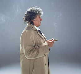 Image showing The senior man with cigar as detective or boss of mafia on gray studio background