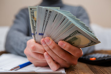 Image showing Caucasian hands counting dollar banknotes on dark wooden table