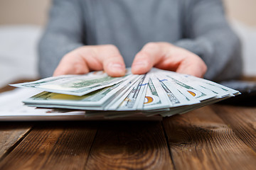 Image showing Caucasian hands counting dollar banknotes on dark wooden table