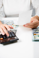 Image showing savings, finances, economy and home concept - close up of hands with calculator counting money and making notes at home