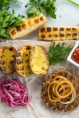 Image showing burger grill with vegetables, sauce on a wooden surface. potatoes and bread