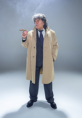 Image showing The senior man with cigar as detective or boss of mafia on gray studio background