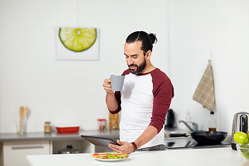 Image showing man with tablet pc eating at home kitchen