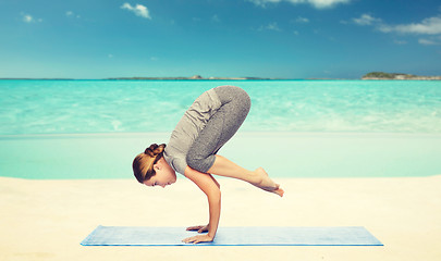 Image showing woman making yoga in crane pose on mat over beach 