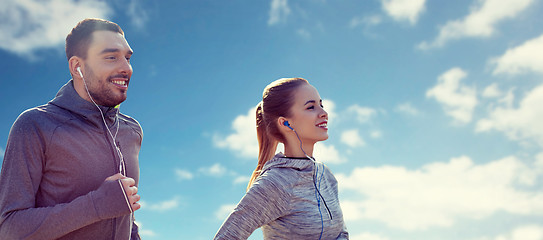 Image showing happy couple with earphones running over blue sky