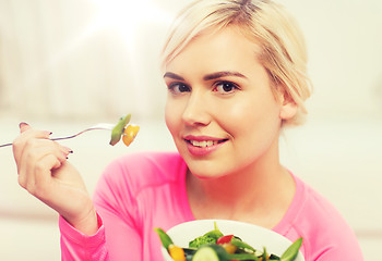 Image showing smiling young woman eating salad at home