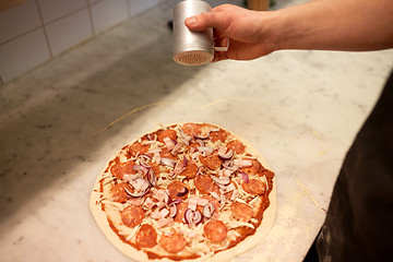 Image showing cook adding pepper to salami pizza at pizzeria