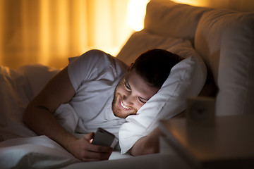 Image showing happy young man with smartphone in bed at night