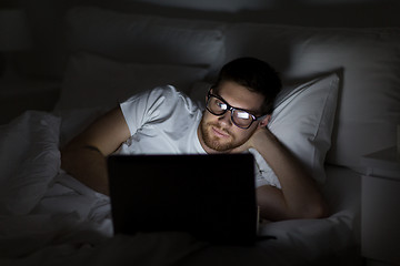 Image showing young man with laptop in bed at home bedroom