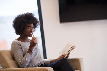 Image showing black woman reading book  in front of fireplace