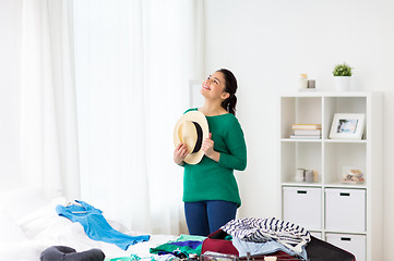 Image showing happy woman with hat packing travel bag at home