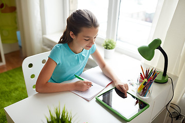 Image showing girl with tablet pc writing to notebook at home