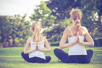 Image showing Mother and daughter doing yoga exercises on grass in the park.