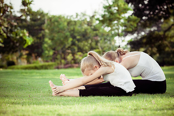 Image showing Mother and daughter doing yoga exercises on grass in the park.